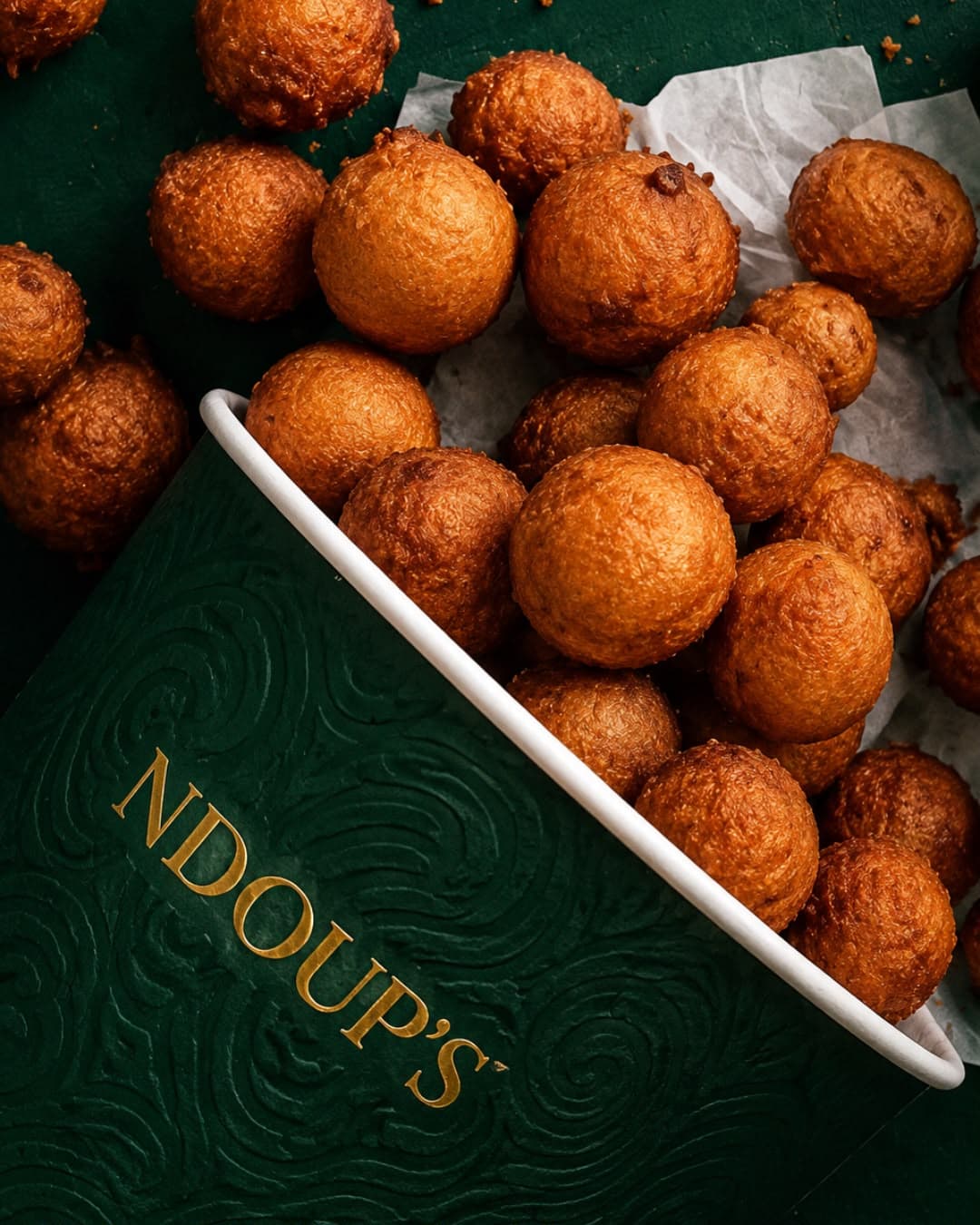 Bucket de beignets NDOUP'S, dorés et moelleux, présenté sur un fond vert et or